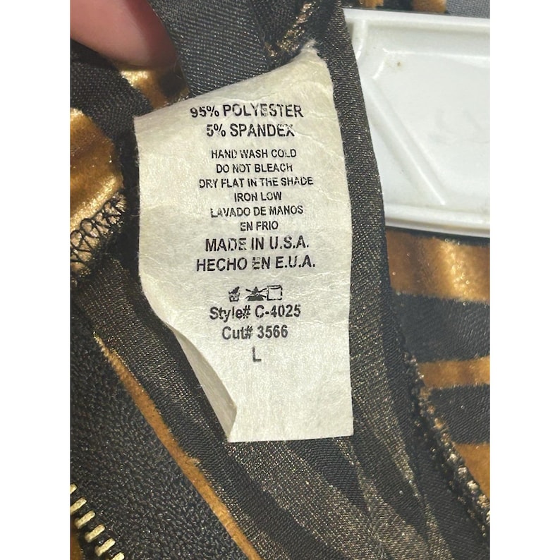 May include: A clothing label with the text "95% POLYESTER 5% SPANDEX" and washing instructions. The label also states "MADE IN U.S.A.". The label is attached to a garment with a black zipper and a gold and black pattern.
