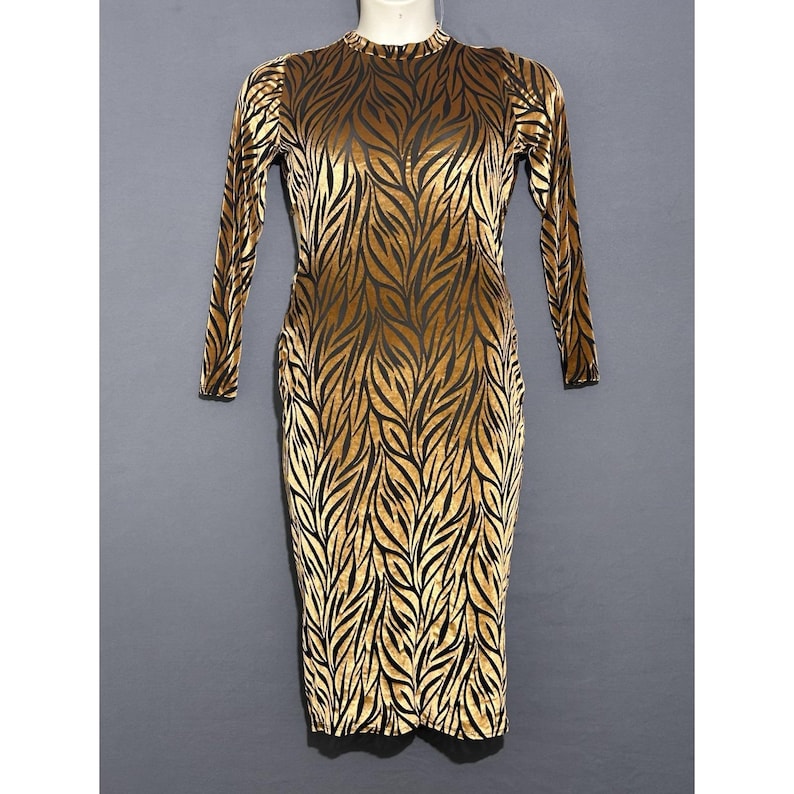 May include: A long-sleeved, knee-length dress with a high neckline. The dress has a pattern of black leaf-like shapes on a gold background. The fabric appears to be velvet, giving the dress a luxurious look. The dress is displayed on a mannequin.