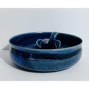May include: A handcrafted, deep blue ceramic bowl with a raised, dark blue elephant figurine in the center. The bowl has a wide, shallow design with a dark blue stripe around the middle. The elephant has its trunk raised.