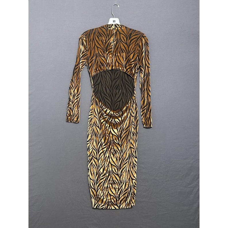 May include: A long-sleeved, figure-hugging dress with a leaf-like pattern in gold and black. The dress has a low back with a dark brown, textured panel. The dress is hanging on a white hanger against a grey background.
