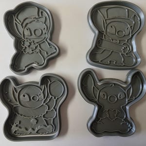 May include: Four gray plastic cookie cutters in the shape of the character Stitch from the animated film Lilo & Stitch. The cutters depict Stitch in various poses, including one with a lei and another with a hat.