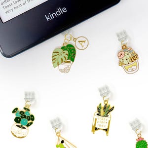 Puede incluir: Nueve clips de marcapáginas de metal dorado con temática de plantas. Los clips presentan una variedad de plantas, incluyendo un cactus, una suculenta, una monstera y un helecho. Los clips están todos unidos a clips de plástico transparente que se pueden usar para sujetar una página en un libro.