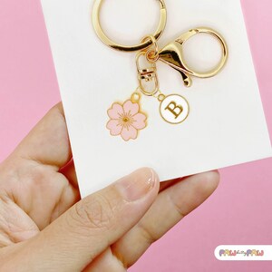 Pink enamel Sakura cherry blossom keychain with gold outline, attached to a gold keyring and an initial charm