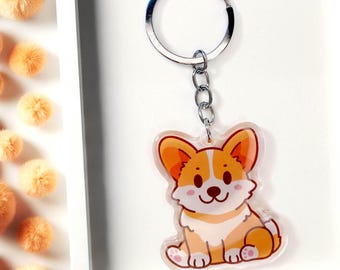 Op de afbeelding: Een heldere acryl sleutelhanger met een cartoon corgi hond met oranje en witte vacht. De sleutelhanger heeft een zilveren metalen ring en ketting. De corgi zit met zijn poten naar voren en heeft een glimlachende uitdrukking.