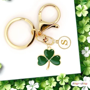 May include: Gold keyring with a green shamrock charm and a white circle charm with the letter "S" on it.
