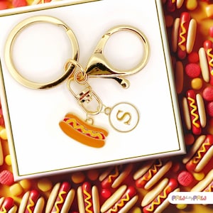 May include: Gold keyring with a hot dog charm and a letter 'S' charm. The keyring is on a white background.