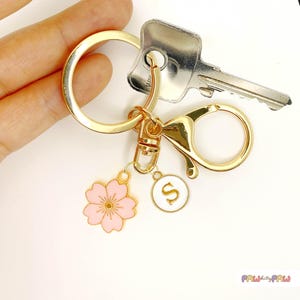 Pink enamel Sakura cherry blossom keychain with gold outline, attached to a gold keyring and an initial charm
