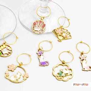 Peut inclure: Huit charmes à vin en or avec différents motifs d'inspiration japonaise. Les charmes représentent un cerf, un éventail, une main tenant une fleur, un chat et un lapin. Les charmes sont parfaits pour ajouter une touche d'élégance à n'importe quel verre à vin.