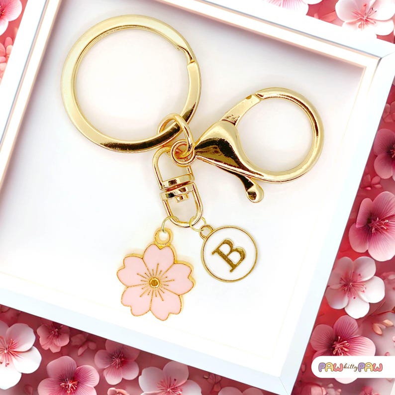 Pink enamel Sakura cherry blossom keychain with gold outline, attached to a gold keyring and an initial charm