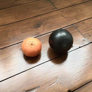May include: An orange tangerine and a black sphere on a wooden surface. The tangerine is round with a textured peel. The black sphere has a smooth, dark surface. The wooden surface has a warm, brown tone.