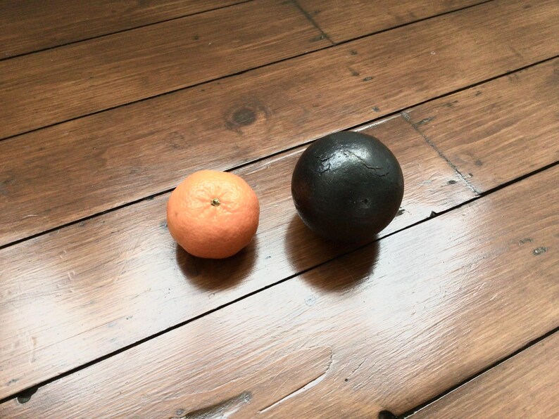 May include: An orange tangerine and a black sphere on a wooden surface. The tangerine is round with a textured peel. The black sphere has a smooth, dark surface. The wooden surface has a warm, brown tone.