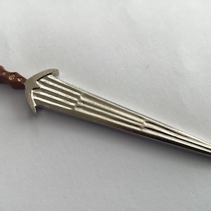 May include: A silver-colored dagger with a brown handle. The blade has a decorative, ridged design.