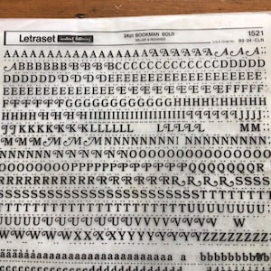 May include: A sheet of Letraset instant lettering in 24pt Bookman Bold font. The sheet contains various uppercase and lowercase letters, numbers, and punctuation marks. The letters are black on a translucent sheet.