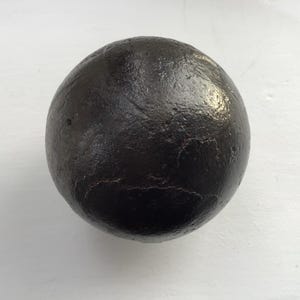 May include: A dark, spherical object with a textured surface. The object is black and appears to be made of a solid material. The sphere is set against a white background.