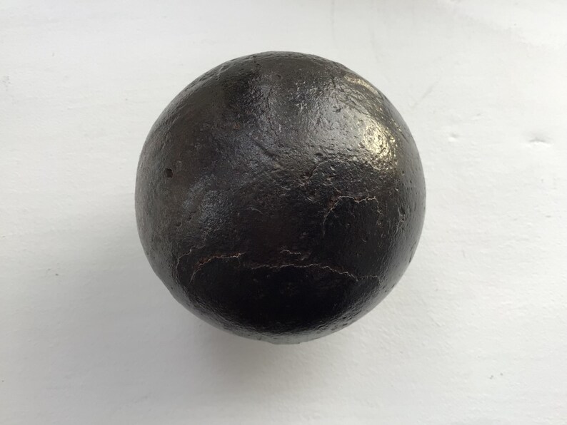 May include: A dark, spherical object with a textured surface. The object is black and appears to be made of a solid material. The sphere is set against a white background.