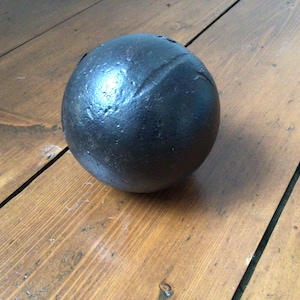 May include: A dark, spherical object with a textured surface, possibly metal. The ball has a visible seam and rests on a wooden surface with visible grain.
