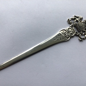 Puede incluir: Abrecartas de plata con un mango adornado que presenta un escudo de armas con un león y una corona.