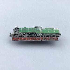 May include: A silver-toned metal enamel pin shaped like a steam locomotive. The train is painted in light green with silver detailing. Below the train, a red rectangular base features the text L.N.E.R. K4 No 3442 THE GREAT MARQUESS.