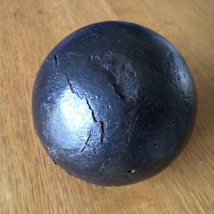 May include: A dark, spherical object with a rough, textured surface and visible cracks. The object is black and appears to be made of a dense material. It rests on a wooden surface.