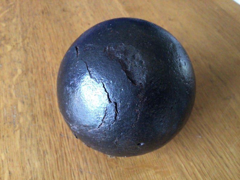 May include: A dark, spherical object with a rough, textured surface and visible cracks. The object is black and appears to be made of a dense material. It rests on a wooden surface.