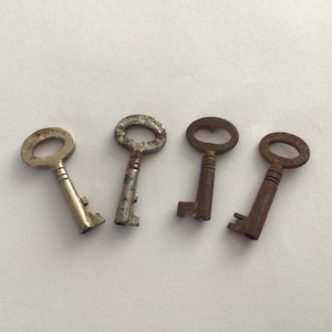 May include: Four antique keys on a white background. The keys are of different designs and sizes, showing signs of age with silver and rusty brown tones. The key heads have various shapes, including oval and heart-shaped designs. The keys are made of metal.