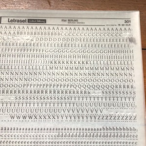 May include: A sheet of Letraset Berling 20pt lettering in a clear plastic sleeve. The sheet contains rows of uppercase and lowercase letters, numbers, and punctuation marks. The letters are black and printed on a white background.
