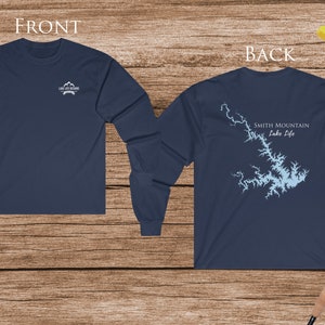 May include: A navy blue long-sleeve t-shirt with a graphic of Smith Mountain Lake and the text "Smith Mountain Lake Life" on the back. The front of the shirt has a small logo with the text "Lake Life at its Finest".
