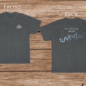 May include: Dark gray t-shirt with the text "LAKE EYE DESIGNS" on the front and a light blue lake map with "OLD HICKORY Lake Life" on the back. The shirt is displayed on a wooden surface with fishing gear.