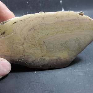 Puede incluir: Un espécimen de piedra natural con apariencia estratificada. La piedra presenta una mezcla de tonos beige, marrón claro y púrpura, con patrones y texturas visibles. La forma irregular y las variaciones de color sugieren una formación geológica.