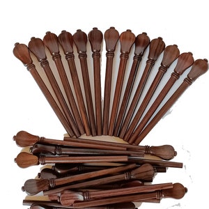 Può includere: Una collezione di bastoncini di legno marrone scuro, ciascuno con una parte superiore decorativa e arrotondata. I bastoncini sono disposti a ventaglio, con alcuni sparsi sotto. La venatura del legno è visibile.