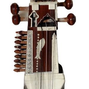 Könnte beinhalten: Ein weißes und braunes Saiteninstrument mit einem Holzkörper und einer weißen Oberseite. Das Instrument hat eine Reihe von Saiten, die über die Länge des Körpers verlaufen, und eine Reihe von Stimmwirbeln an der Oberseite. Das Instrument heißt "Sitar" und ist ein traditionelles indisches Musikinstrument.