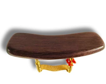 May include: A dark brown violin shoulder rest with a curved wooden pad and gold-colored metal supports. A small red ribbon is attached to the side. The rest is designed to provide comfort and support while playing the violin.