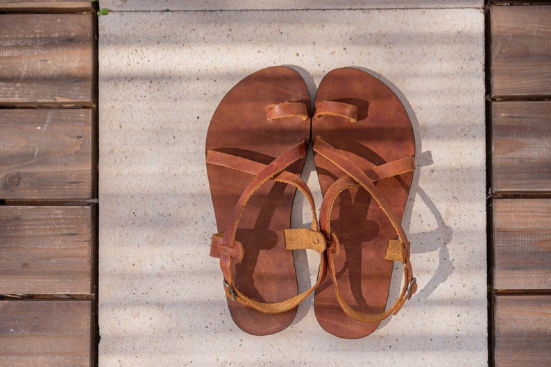 May include: A pair of brown leather sandals with criss-cross straps and a toe loop.
