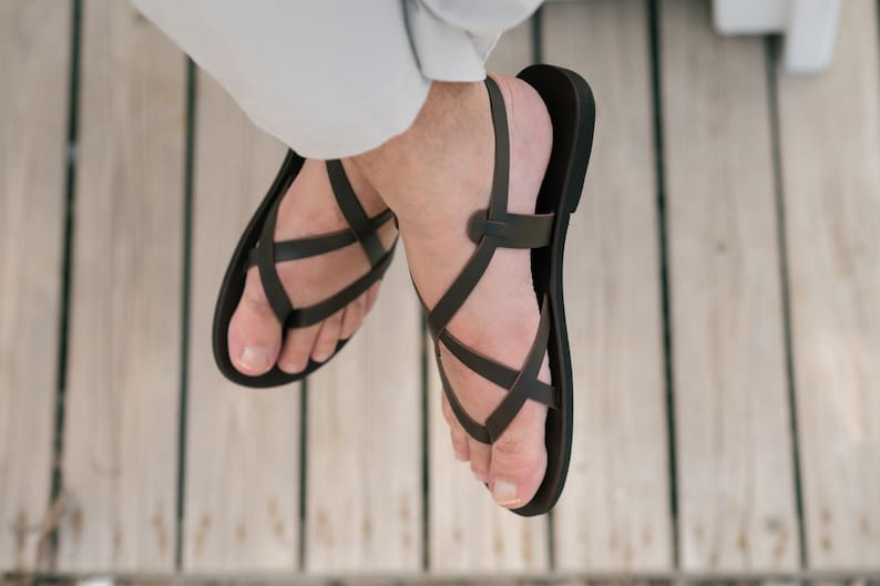 May include: A pair of black leather sandals with criss-cross straps. The sandals are worn on a person's feet.