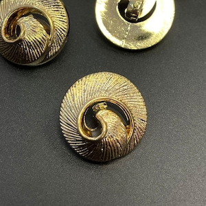 Peut inclure: Un ensemble de boutons dorés avec un motif en spirale. Les boutons sont ronds et ont une surface texturée en relief.
