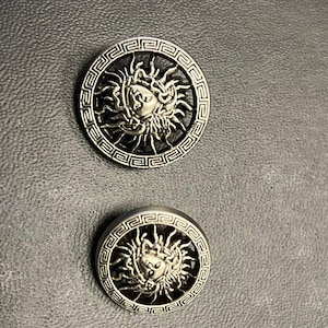 May include: Two silver-toned buttons featuring a Medusa head design encircled by a Greek key pattern.