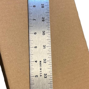May include: A metal ruler with inch markings, numbered from 1 to 36, is displayed against a brown cardboard background. The ruler is marked "MADE IN U.S.A."
