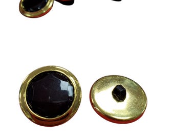 Könnte beinhalten: Eine Sammlung runder Knöpfe mit einem polierten goldfarbenen Metallrand und einer glatten, dunkelbraunen Mitte. Die Vorderansicht zeigt die reflektierende dunkle Oberfläche, während die Rückseite das goldene Metallfinish und eine schwarze Öse zeigt.