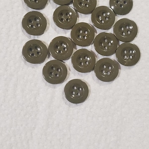 May include: A collection of olive green buttons with four holes each. The buttons are round and have a slightly glossy finish. They are scattered on a white, textured surface.