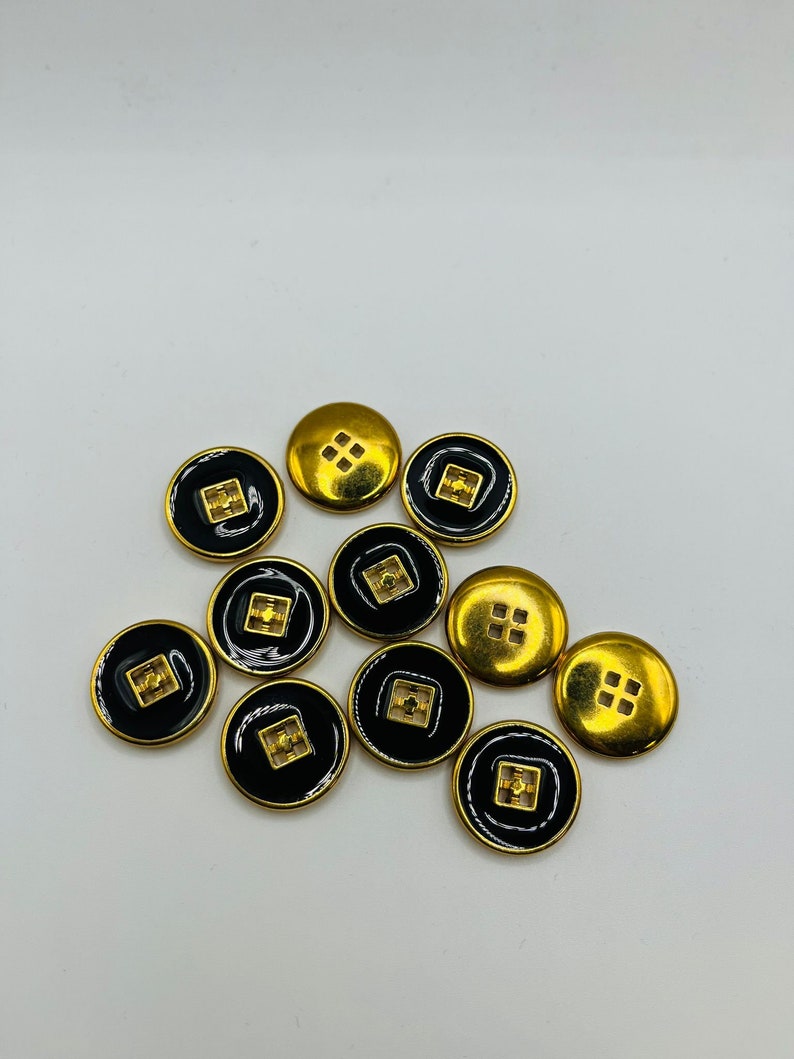 Peut inclure: Dix boutons ronds noirs et dor&eacute;s. Les boutons ont un motif carr&eacute; au centre.
