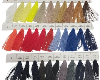 Könnte beinhalten: Eine Farbkarte mit drei Reihen nummerierter Garnproben. Jede Reihe zeigt verschiedene Stickgarnschattierungen in einem Farbverlauf, darunter Weiß, Gelb, Beige, Braun, Orange, Rot, Blau, Grau und Schwarz, jeweils mit Beschriftung.