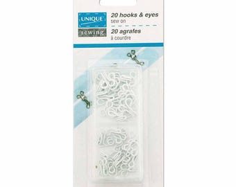 Könnte beinhalten: Eine Packung mit 20 weißen Haken und Ösen zum Annähen von Unique Sewing. Die weiß-blaue Verpackung trägt die Aufschrift 20 hooks & eyes sew on und rust resistant/brass. Der durchsichtige Kunststoffbehälter enthält die kleinen Metallverschlüsse.