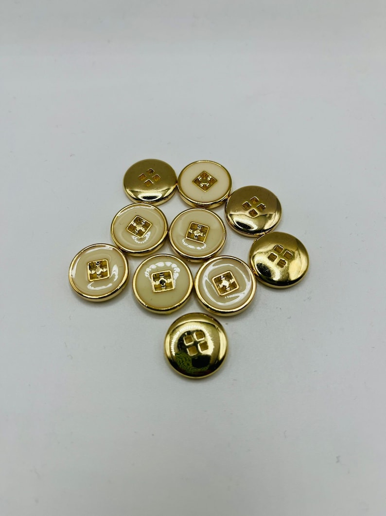 Peut inclure: Un groupe de dix boutons dor&eacute;s avec un centre blanc. Les boutons ont un motif carr&eacute; au centre.