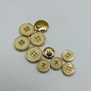 Peut inclure: Un ensemble de dix boutons de couleur or avec un centre blanc. Les boutons ont un motif carr&eacute; au centre.