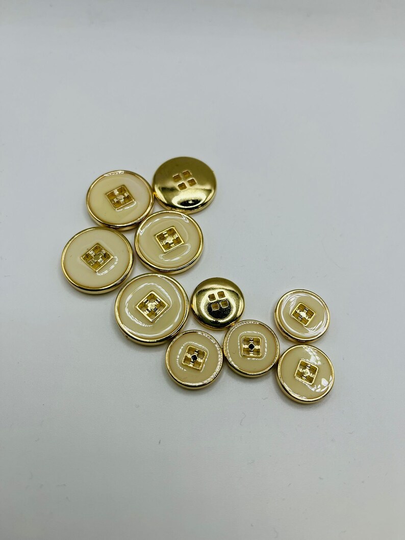 Peut inclure: Un ensemble de dix boutons de couleur or avec un centre blanc. Les boutons ont un motif carr&eacute; au centre.