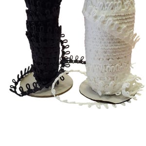 May include: Two spools of decorative trim, one black and one white, are displayed against a white background. The trim has a looped design and is wound around cardboard spools. The trim is ideal for sewing and crafting projects.