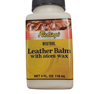 Może przedstawiać: Biała butelka neutralnego balsamu do skóry Fiebing's z czarną zakrętką. Etykieta jest żółta z napisem "Leather Balm with atom wax". Butelka zawiera 118 ml produktu.