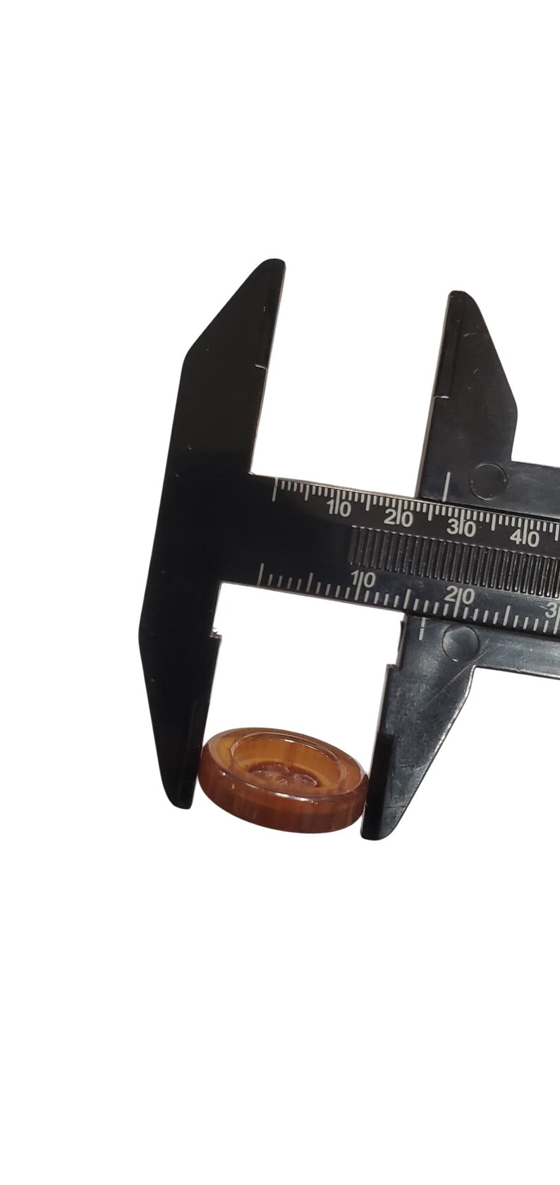May include: A brown, oval button is measured with a black caliper. The button is made of a translucent material. The caliper is marked with measurements in centimetres and millimetres.