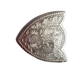 Peut inclure: Boucle de ceinture décorative en métal argenté avec un motif floral et volute complexe. La boucle a une forme incurvée avec un bord festonné, et un tournesol est visible au centre du motif.
