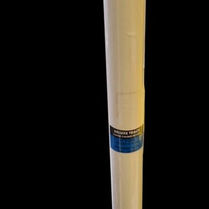 May include: A roll of Deluxe Trace paper, wrapped in clear plastic. The paper is a light cream colour, and a blue and white label is visible. The roll is against a black background.